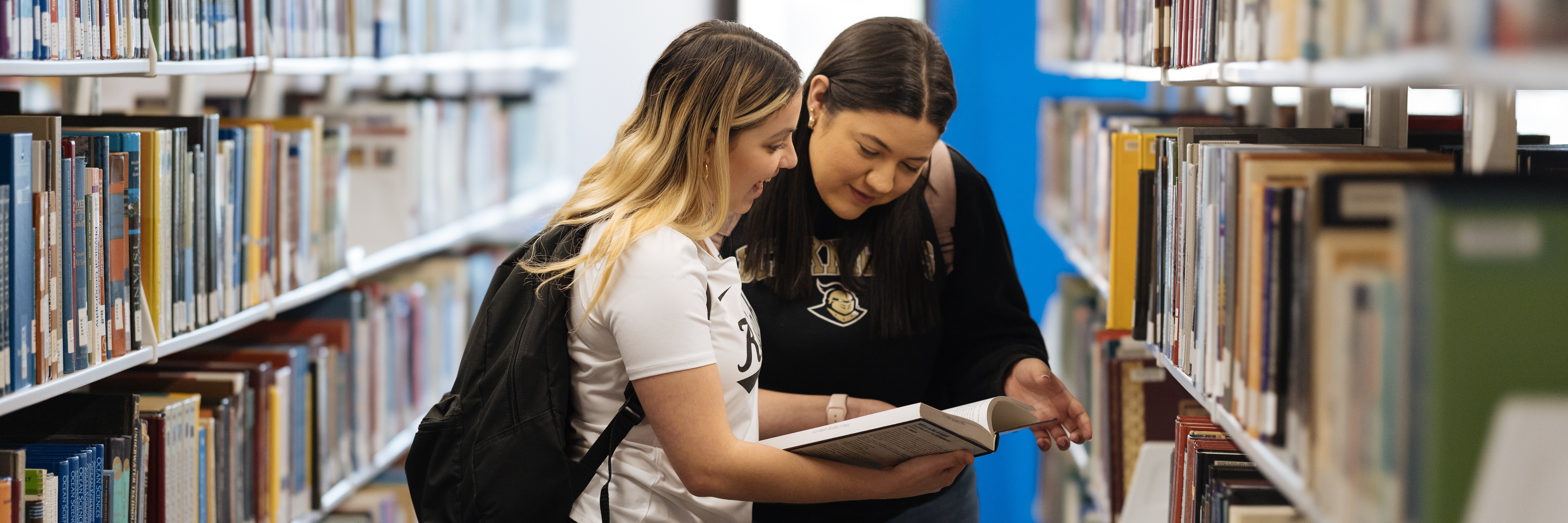 Two students look at a book in the John C. Hitt Library.