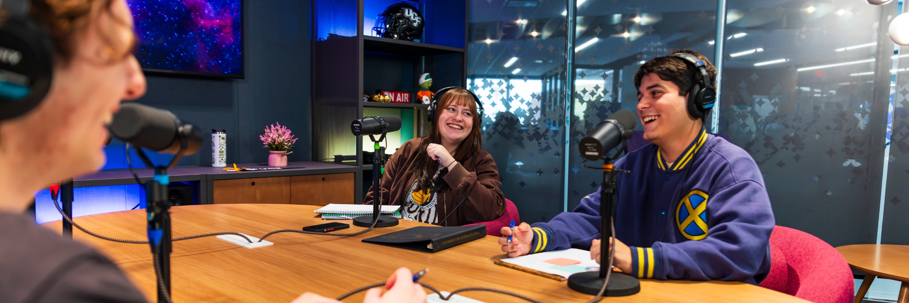 Students smile and laugh in UCF's podcast studio with headphones in